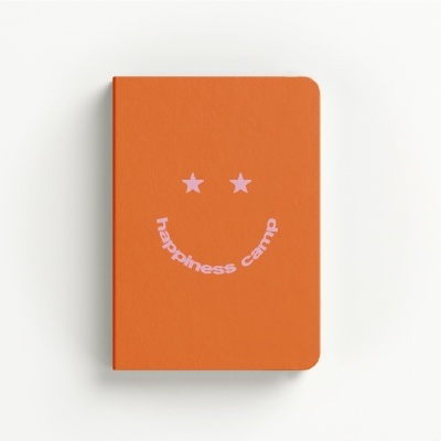 Orange notebook with pink smiley face and happiness camp text