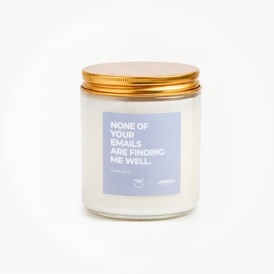 White candle in glass jar with gold lid and blue label with white text