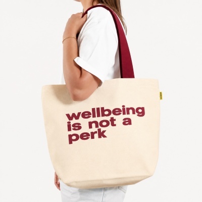 Beige canvas tote bag with red handles and text, worn on shoulder