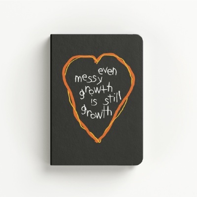Black notebook with orange heart outline and white handwritten text on front cover