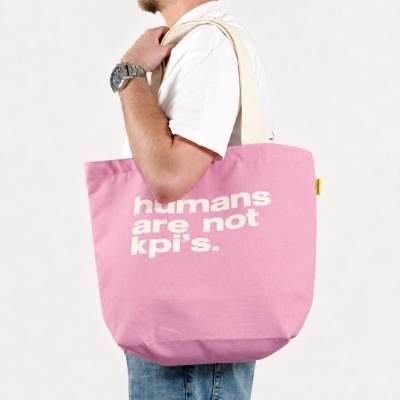 Person carrying a pink canvas tote bag with the text humans are not kpis. printed on it.
