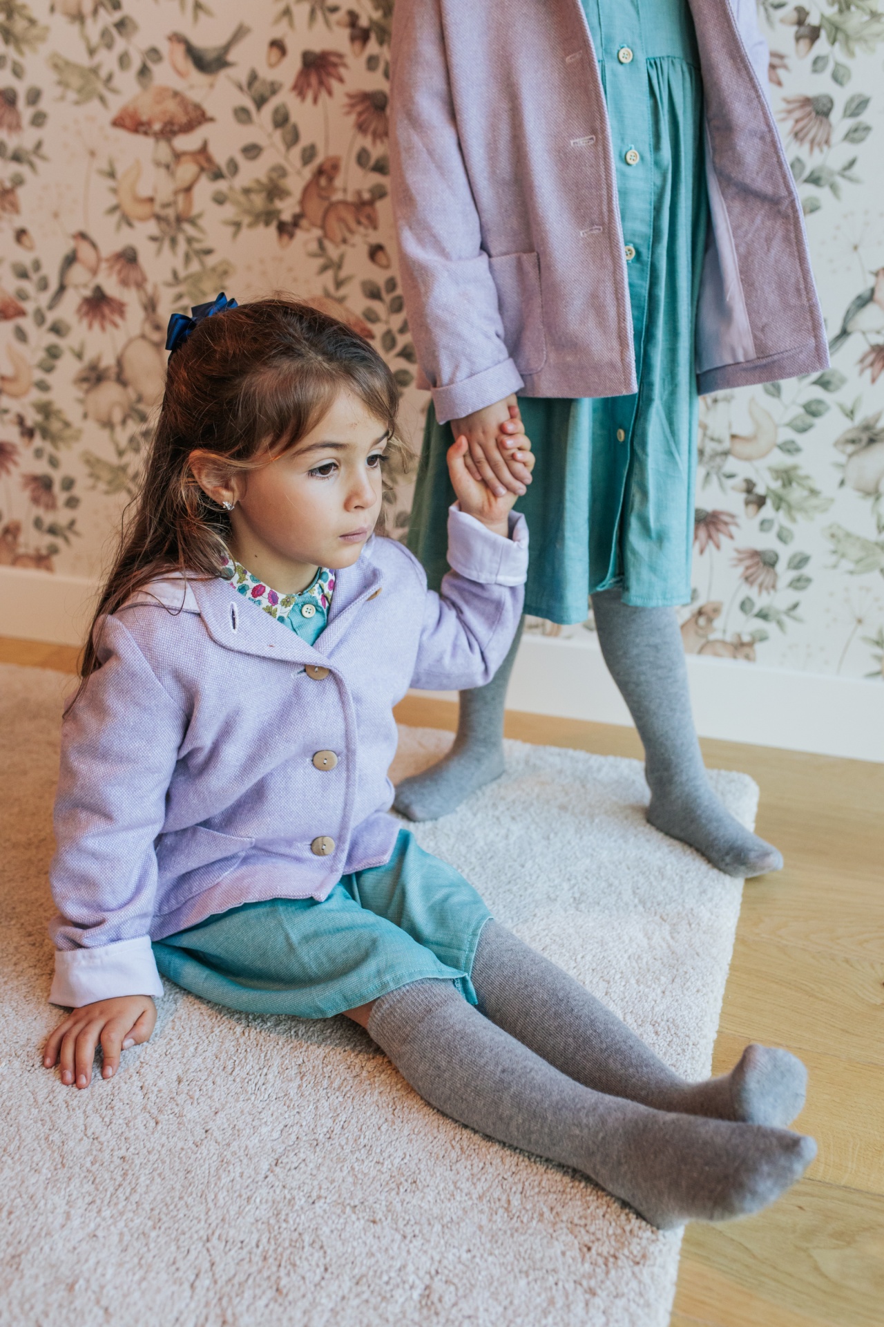 Casaco Bosco Crianças com vestidos verdes e casacos lilás em ambiente com papel de parede floral