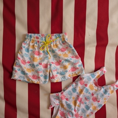 Conjunto de roupa de criança com estampa de caranguejos sobre tecido às riscas vermelhas e bege.