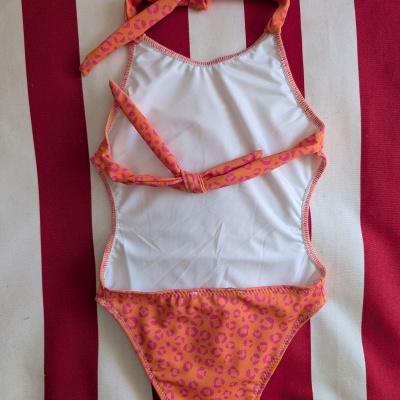 Fato de banho branco e laranja com padrão rosa, sobre tecido riscado vermelho e branco