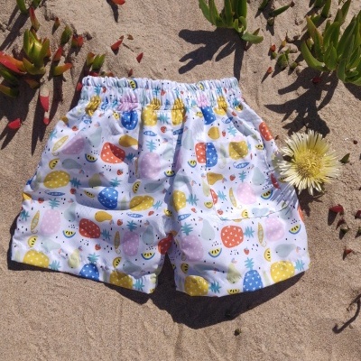 Calções de criança com padrão colorido de frutas na areia com plantas verdes e flor amarela