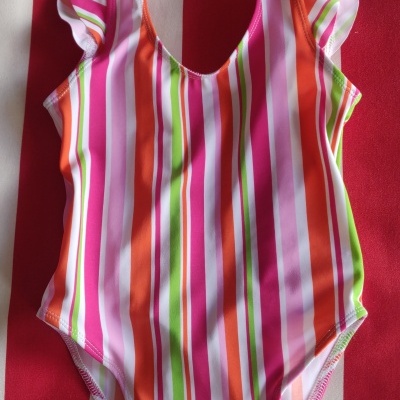 Fato de banho listrado colorido para criança sobre tecido riscado vermelho e branco.