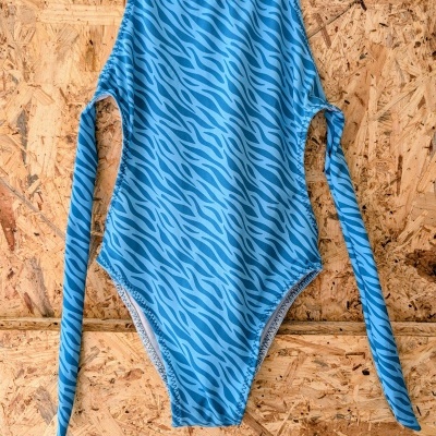 Fato de banho azul com padrão abstrato pendurado numa parede de madeira OSB