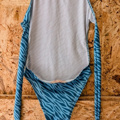 Fato de banho azul com riscas pretas pendurado num painel de madeira OSB