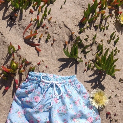 Calções de praia azuis claros com padrão floral rosa e verde na areia