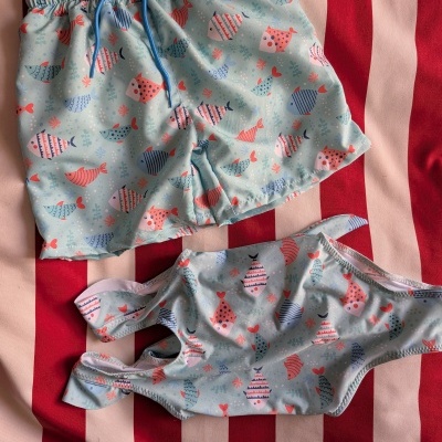Roupa de banho infantil com padrão de peixes coloridos sobre fundo riscado vermelho e branco