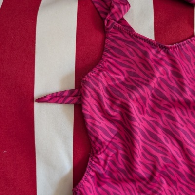 Fato de banho rosa com padrão zebrado colocado sobre tecido riscado vermelho e branco
