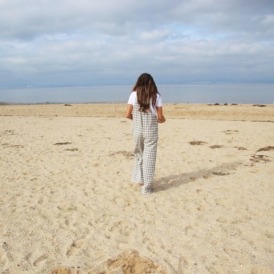 Mulher de costas na praia com macacão aos quadrados e T-shirt branca