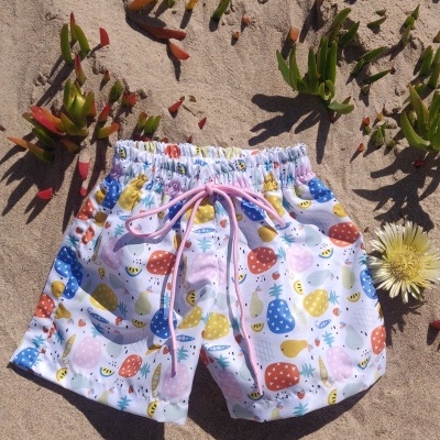 Calções de banho infantis coloridos na areia junto de plantas e flor amarela