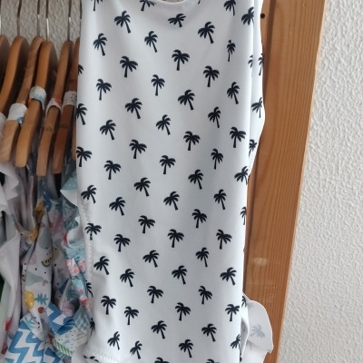 Fato de banho uma peça branco com palmeiras pretas e alças pretas num cabide de madeira