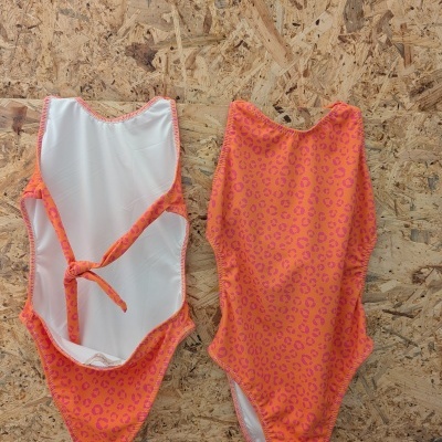 Dois fatos de banho laranja com padrão de manchas rosas, um virado do avesso mostrando forro branco e cordão, outro do direito