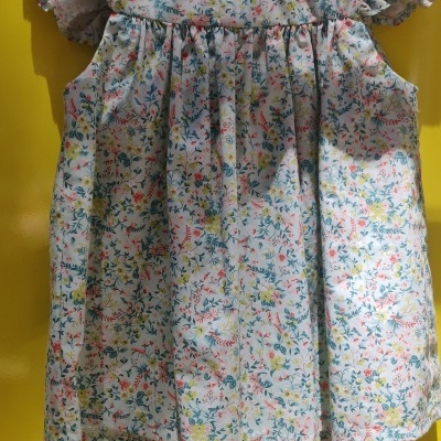 Vestido floral infantil branco com mangas curtas onduladas num cabide de madeira