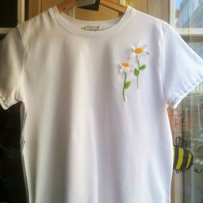 T-shirt branca com bordado de flores e etiqueta pendurada num cabide