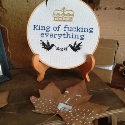 Quadro de bordado redondo com texto e coroa, sobre suporte de madeira