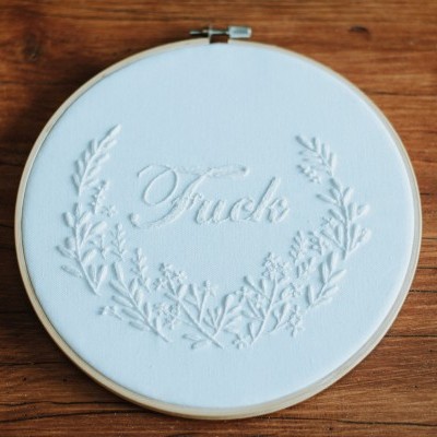 Bastidor bordado com palavra e desenho floral em relevo sobre madeira