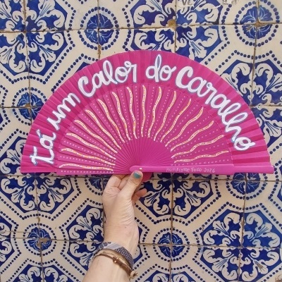Leque cor-de-rosa com texto branco e desenho de raios de sol perante azulejos azuis e brancos