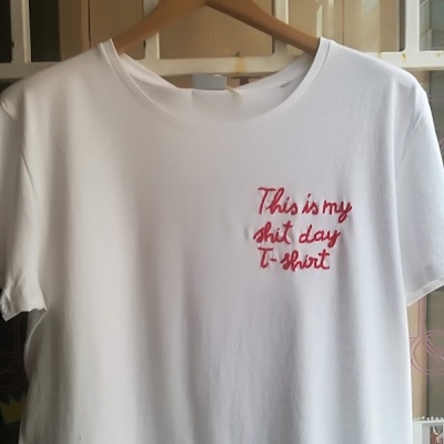 T-shirt branca com texto bordado vermelho pendurada em cabide