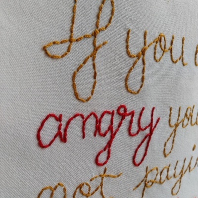 Tecido branco bordado com texto em linhas amarelo mostarda e vermelho