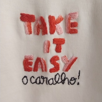 Tecido branco com bordado colorido a dizer TAKE IT EASY o caralho!