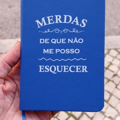Caderno azul com texto branco impresso segurado à mão sobre calçada e rua