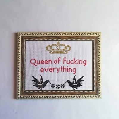 Bordado em ponto cruz com moldura dourada, texto em inglês e desenhos de coroa e aves sobre tecido branco