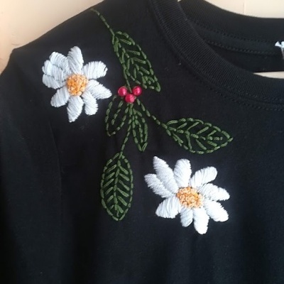 Camisola preta com bordados florais coloridos num cabide