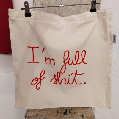 Saco de tecido bege com frase bordada a vermelho pendurado num cabide