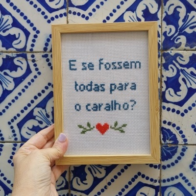 Quadro com bordado e texto em azul com coração vermelho sobre azulejos azuis e brancos.
