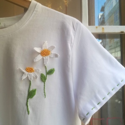 Camiseta branca com flores bordadas e detalhes verdes na manga