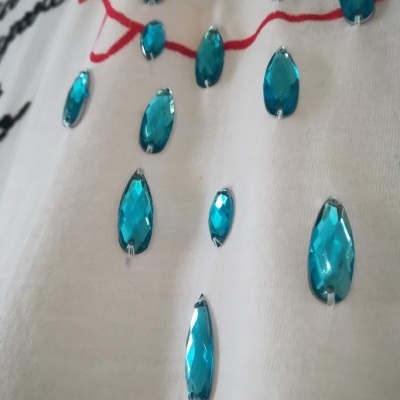 Tecido branco com pedras decorativas azuis aplicadas e linhas vermelhas e pretas desenhadas