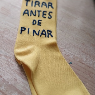 Meia amarela com texto bordado azul sobre superfície de madeira