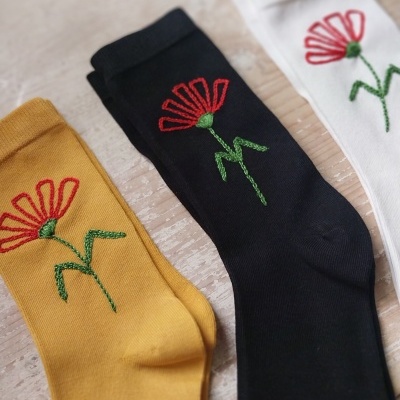 Meias coloridas com flor vermelha bordada sobre madeira clara