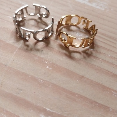 Dois anéis metálicos, um prateado e outro dourado, com palavras recortadas no aro, sobre madeira clara.