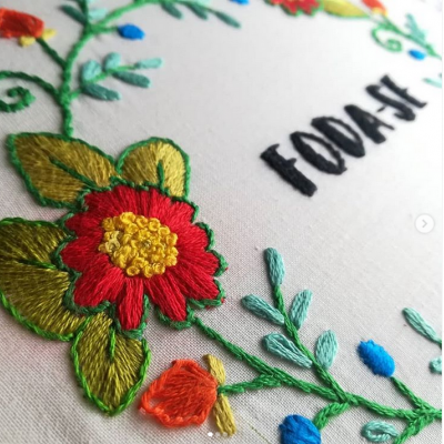 Bordado colorido com flores e texto 'FODASE' em tecido branco