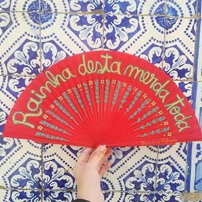 Leque vermelho com texto e desenhos florais segurado diante de azulejos azuis e brancos