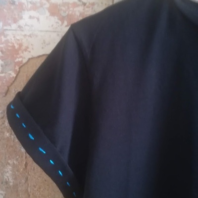 T-shirt preta com manga dobrada e pontos azuis numa parede envelhecida