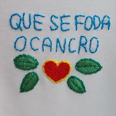 Bordado em tecido branco com frase em azul, coração vermelho e folhas verdes