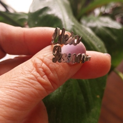 Anel de prata personalizado com nomes segurado a dedo em frente a folha verde