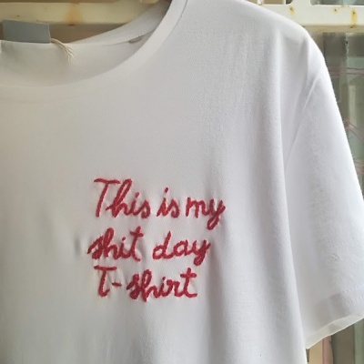 T-shirt branca com bordado vermelho pendurada num cabide