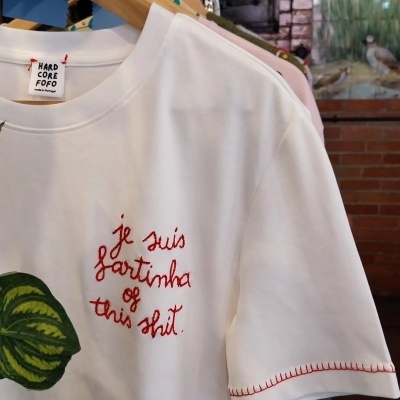 T-shirt branca com bordado vermelho e costura decorativa na manga pendurada num cabide