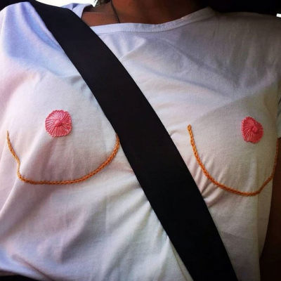 T-shirt branca com bordados laranja e círculos cor-de-rosa no peito e cinto de segurança preto