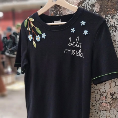 T-shirt preta com bordados de flores azuis e texto 'bela merda'