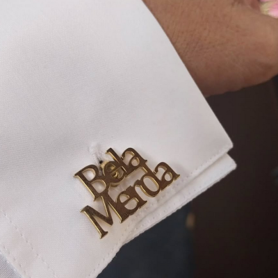 Abotoadura dourada com texto 'Bela Merda' numa camisa branca