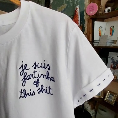 T-shirt branca com bordado azul escuro e pontos decorativos na manga num ambiente interior