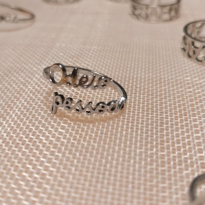 Anel em metal prateado com a frase Odeia pessoal em relevo sobre tecido bege