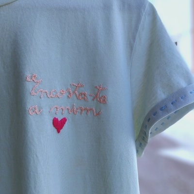 T-shirt branca com bordado cor-de-rosa e vermelho num cabide de madeira